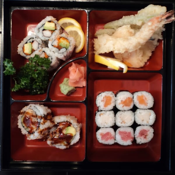A bento box filled with various sushi rolls, tempura, ginger, and wasabi.