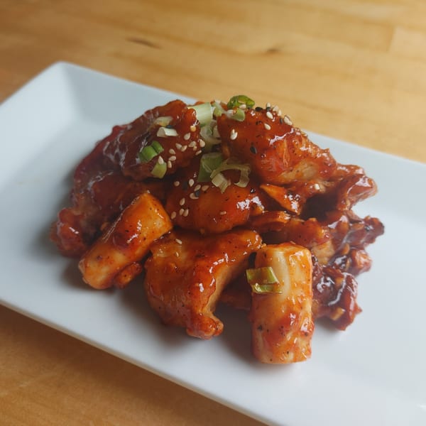 Spicy Korean fried chicken and tteokbokki rice cakes, garnished with green onions and sesame seeds.