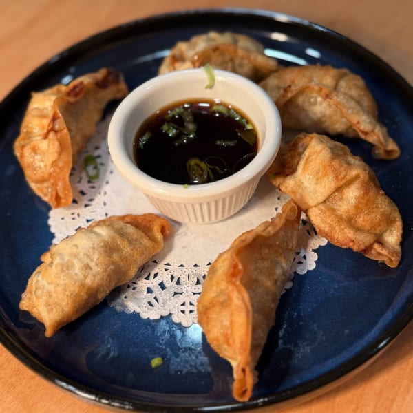 Six crispy fried dumplings arranged around a small bowl of soy sauce with green onions on a blue plate.