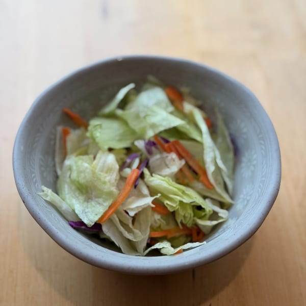 A light gray bowl filled with a fresh garden salad of lettuce, shredded carrots, and purple cabbage.