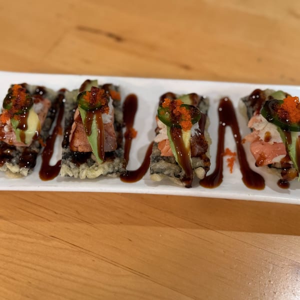 Four pieces of sushi with salmon, avocado, jalapeño, and roe, drizzled with sauce.