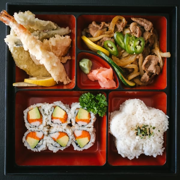 A bento box with tempura, beef and onions, California rolls, and white rice.