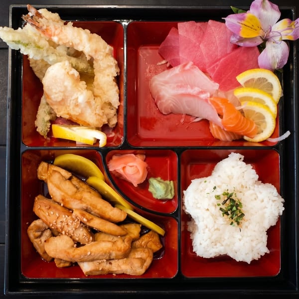 A bento box with tempura, sashimi, teriyaki chicken, rice, pickled ginger, and wasabi.